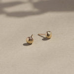 yellow gold textured pebble stud earrings on beige surface with leaf shadows