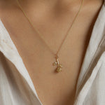 Gold necklace with a rose stem pendant worn by a person in a light-colored shirt.