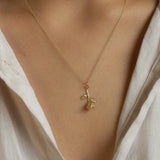 Gold necklace with a rose stem pendant worn by a person in a light-colored shirt.