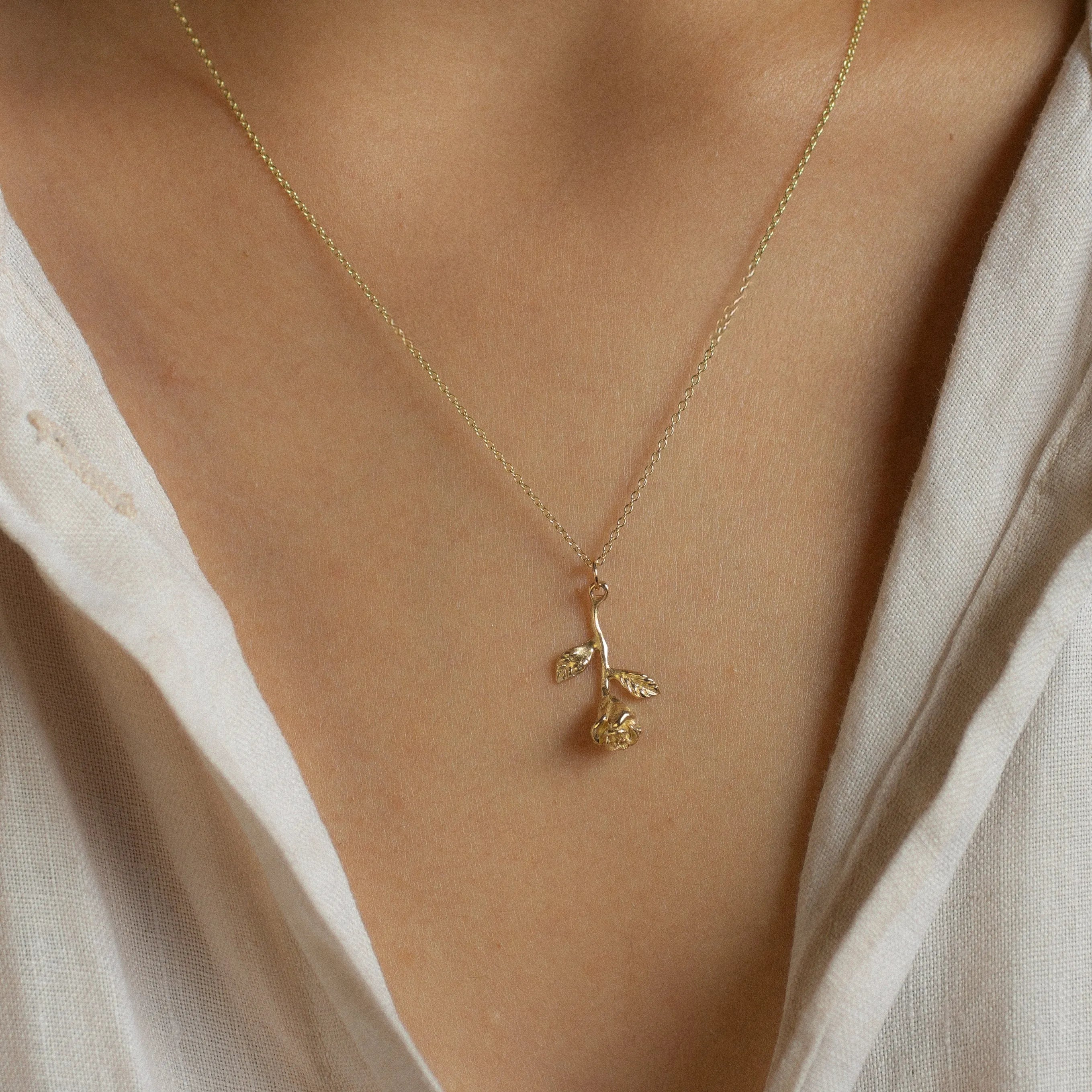 Gold necklace with a rose stem pendant worn by a person in a light-colored shirt.