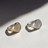 Two st christopher rings, one st christopher ring in gold and one silver, on a light surface with a soft shadow.