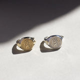 Two saint christopher signet rings, one gold and one silver, on a light surface with a soft shadow.