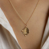 Gold necklace with a pendant worn by a person in a white shirt.