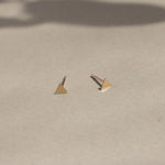 solid yellow gold triangle stud earrings on beige surface with leaf shadows