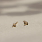 yellow gold triple dot stud earrings on beige surface with leaf shadows