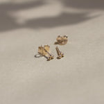 solid yellow gold triple dot stud earrings with butterfly backs on beige surface with leaf shadows
