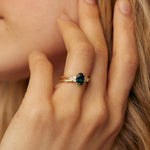 Close-up of a hand wearing a gold ring with a green gemstone, touching hair.