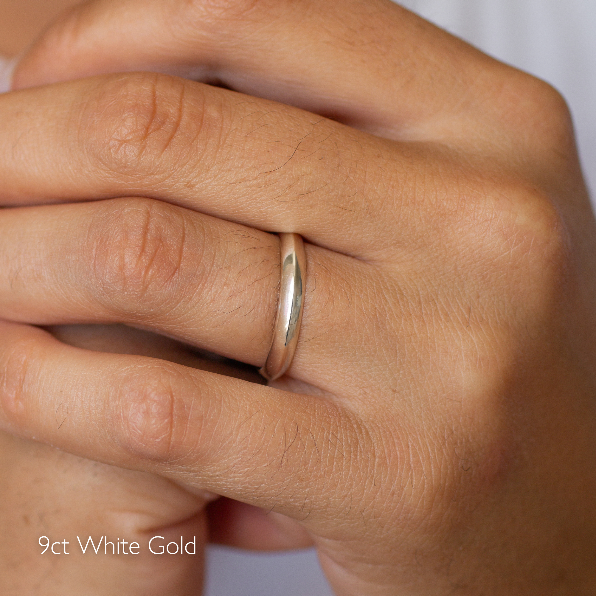 Close-up of a hand wearing a 9ct white gold ring with knife edge profile on a plain background