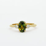 gold engagement ring with green yellow sapphire and round diamonds on a white background