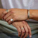 close up of mans hands wearing silver chunky bangle, handwriting ring, full moon ring and saint christopher signet ring
