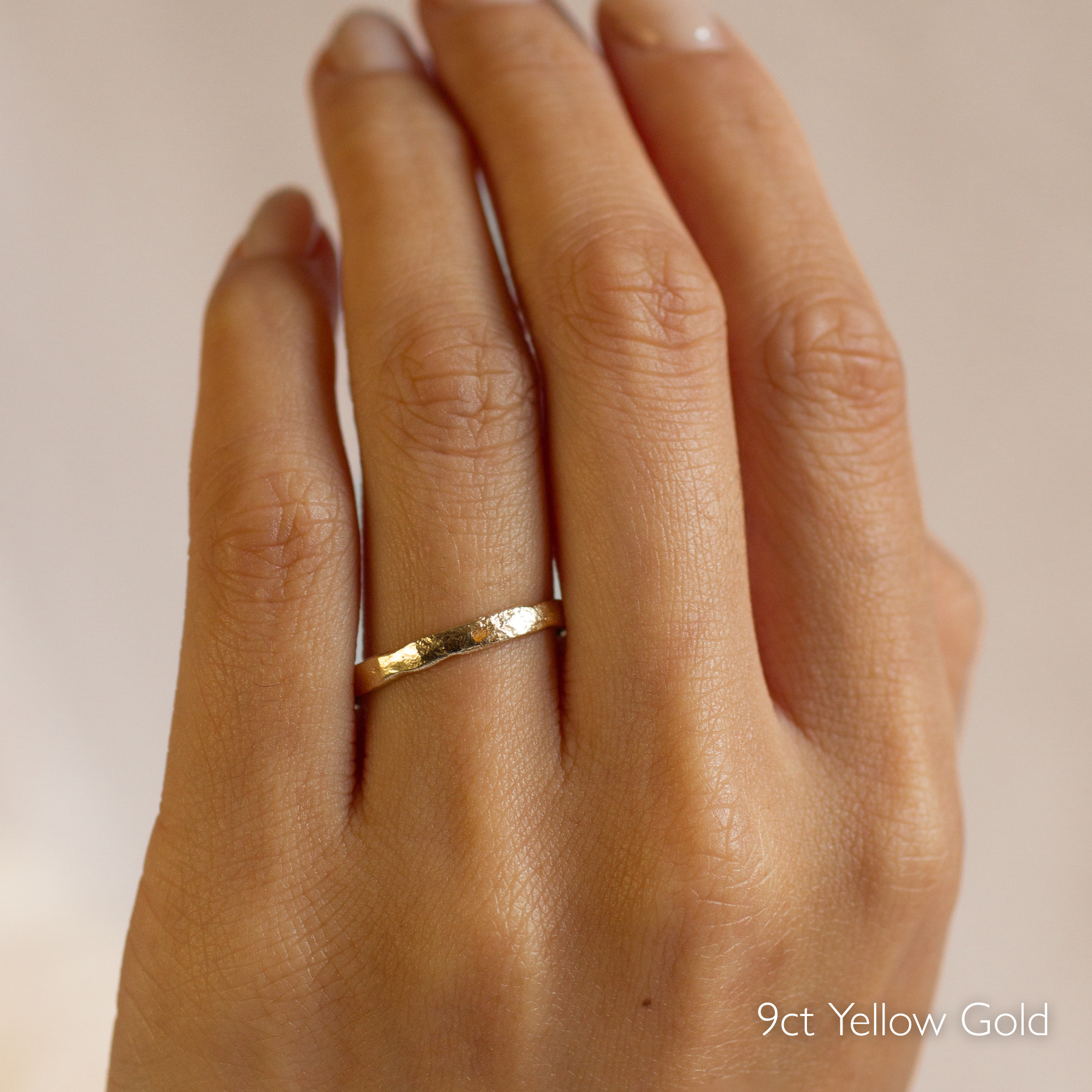 Gold organic rustic wedding ring with 2mm width on a hand with '9ct Yellow Gold' text