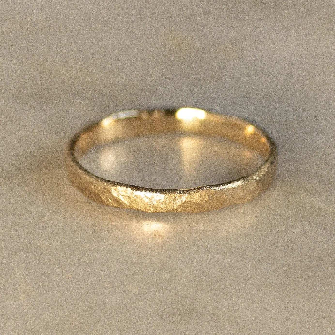 Gold rustic wedding ring with uneven edges on a marble surface