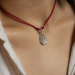 Close-up of a person wearing a red cord necklace with a silver pendant.