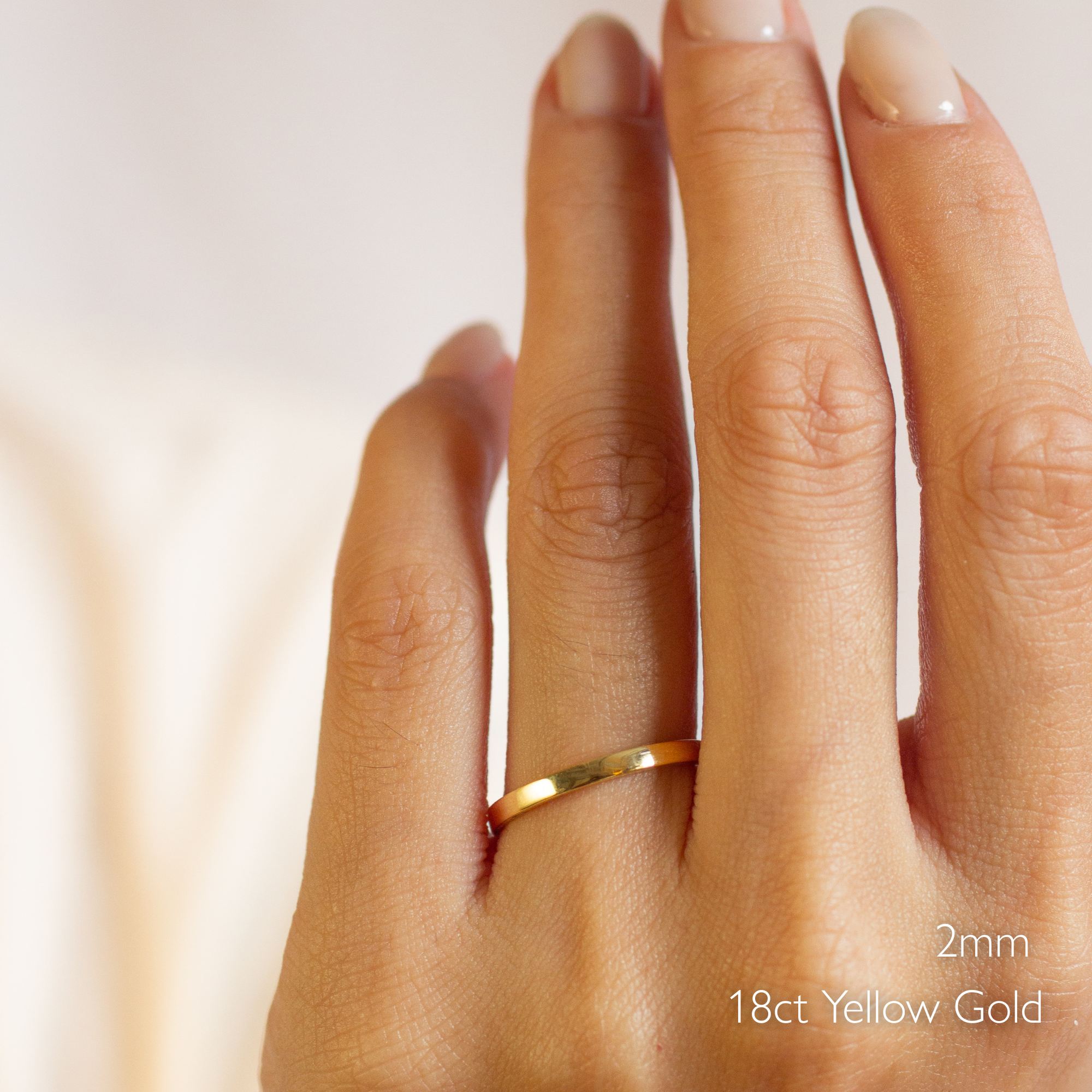 Gold flat wedding ring on a hand with '2mm' and '18ct Yellow Gold' text.