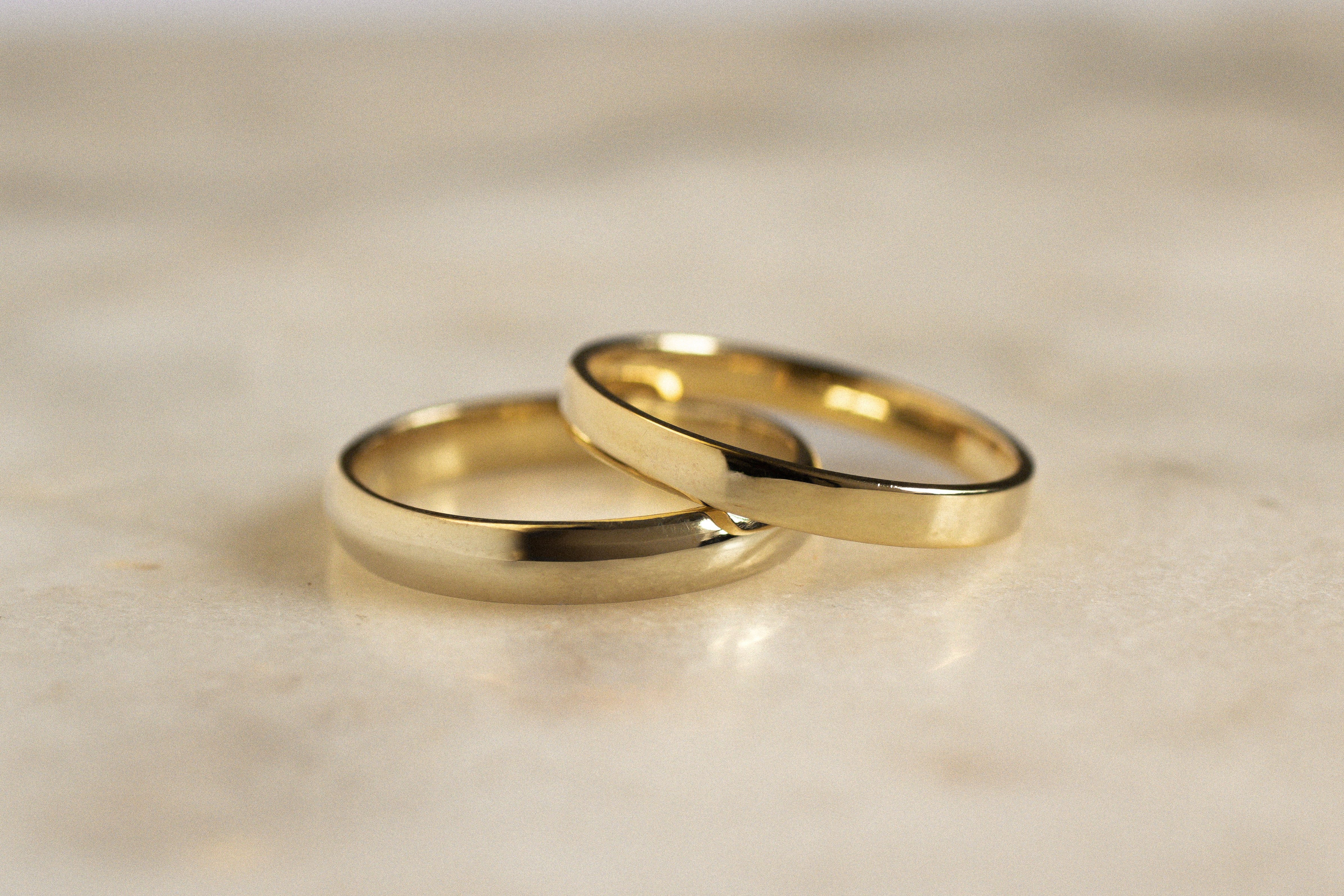 flat polished wedding ring leaning slanted on a d shaped wedding ring in yellow gold