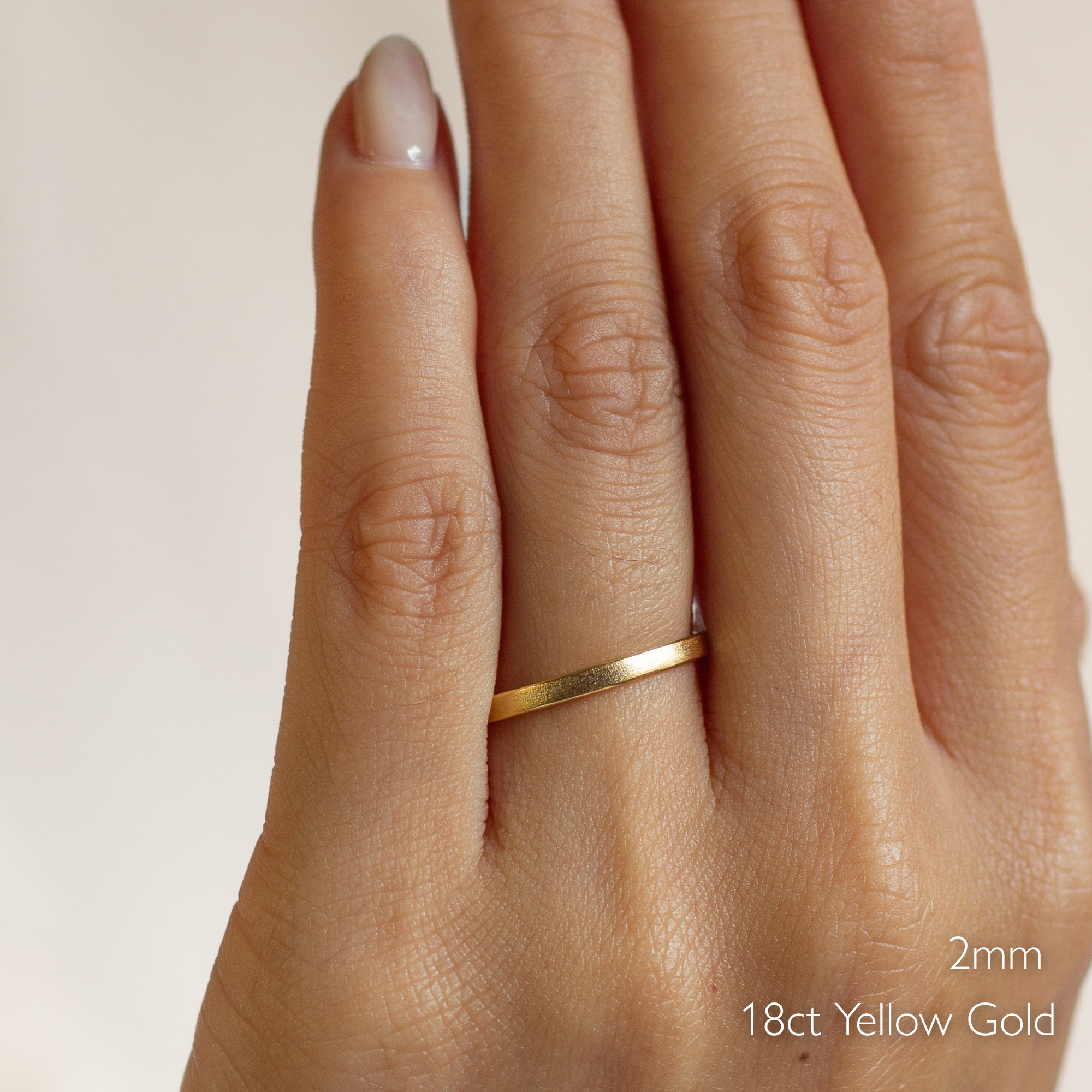 Gold satin wedding ring on a hand with '2mm' and '18ct Yellow Gold' text.