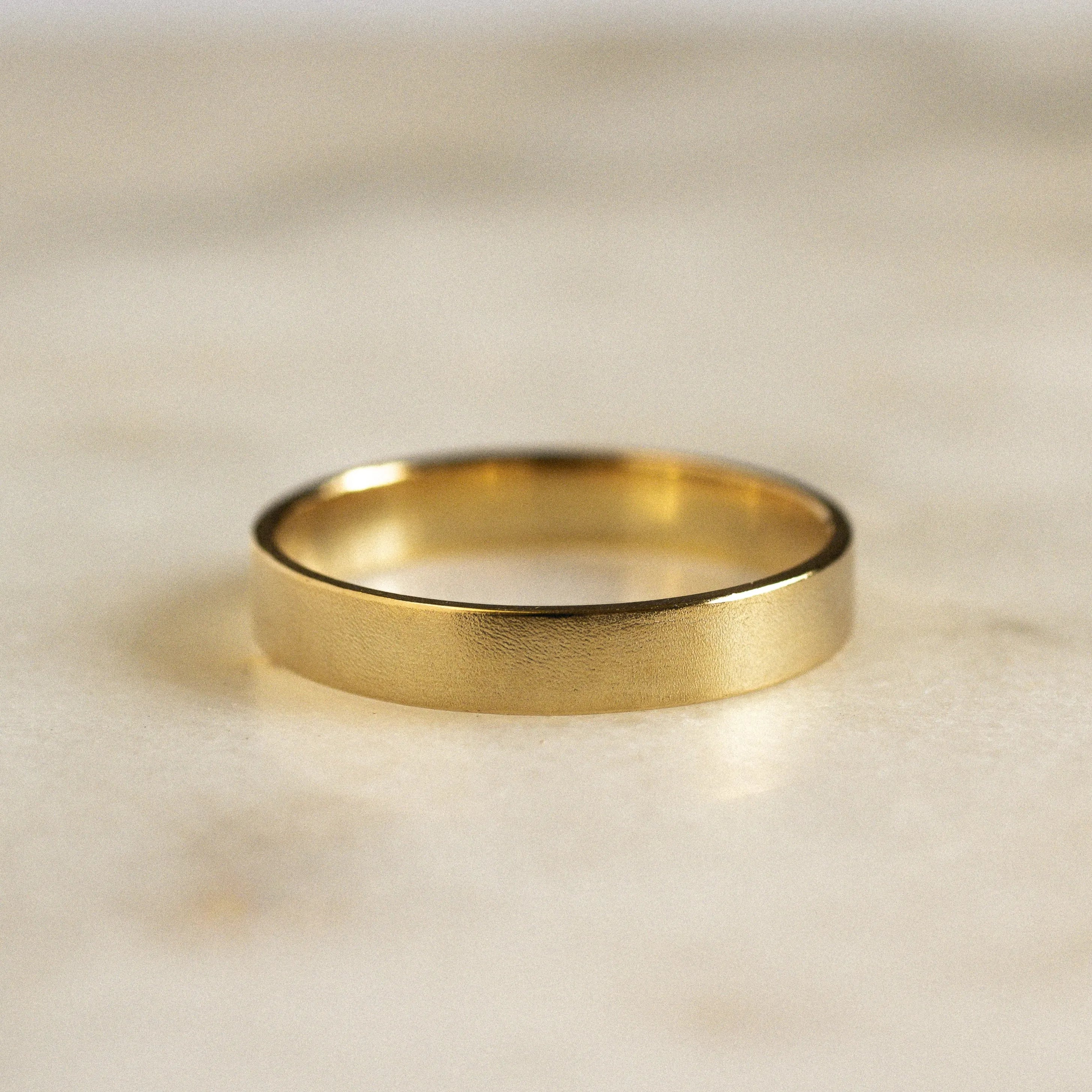 gold wedding ring with blurred satin texture in flat shape on marble surface