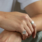 close up of mens hand wearing silver saint christopher ring and raw band ring