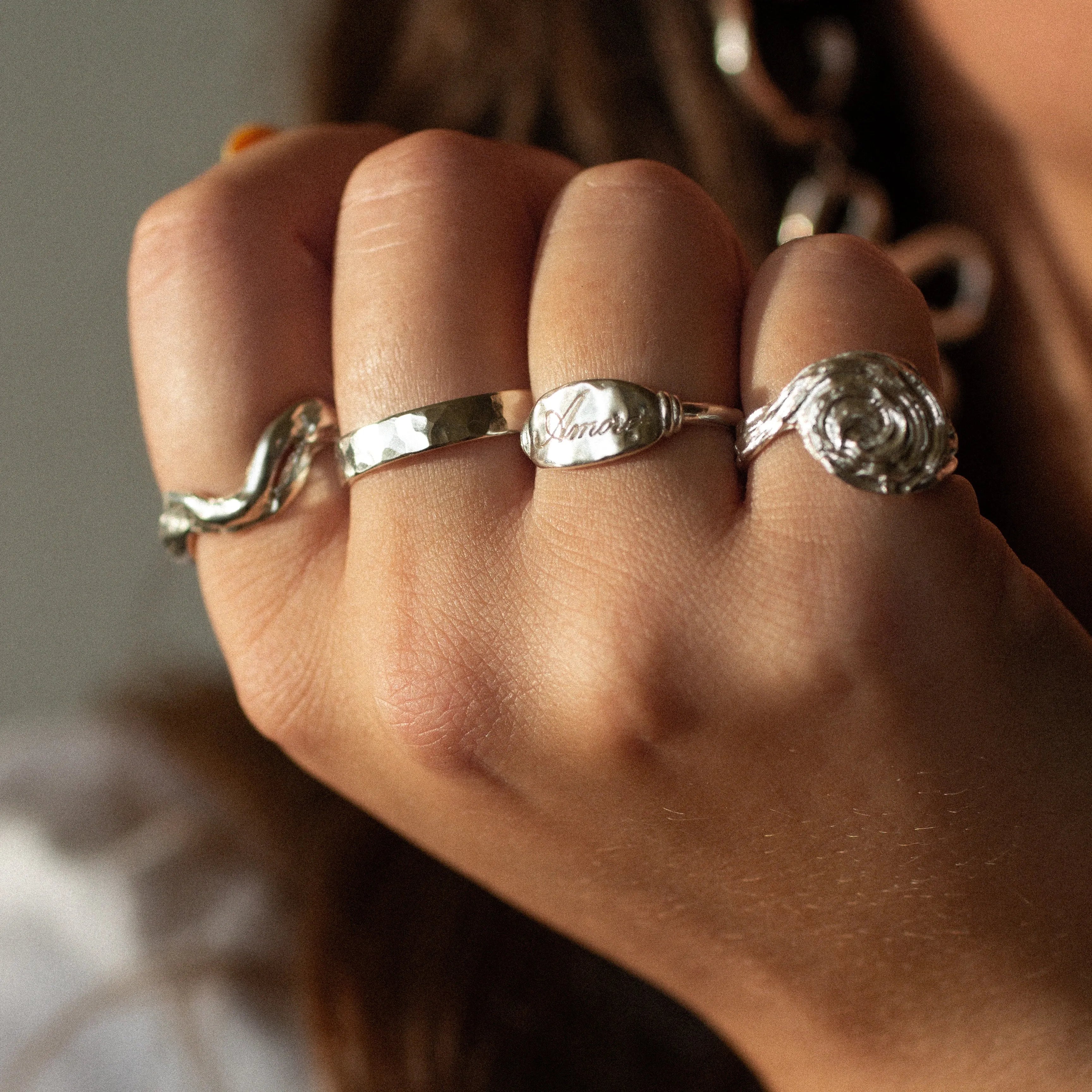 Close-up of a hand wearing multiple silver rings with intricate designs.