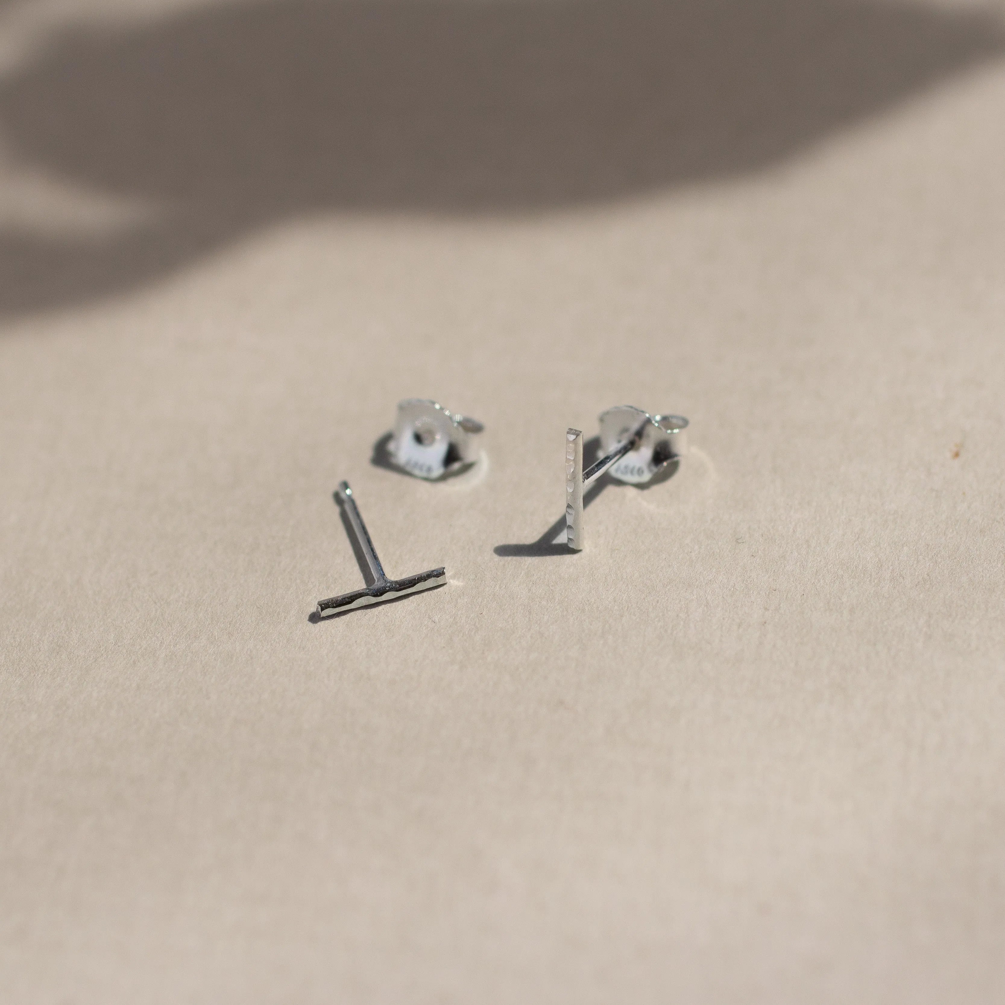 sterling silver hammered bar stud earrings with butterfly backs on beige surface with leaf shadows