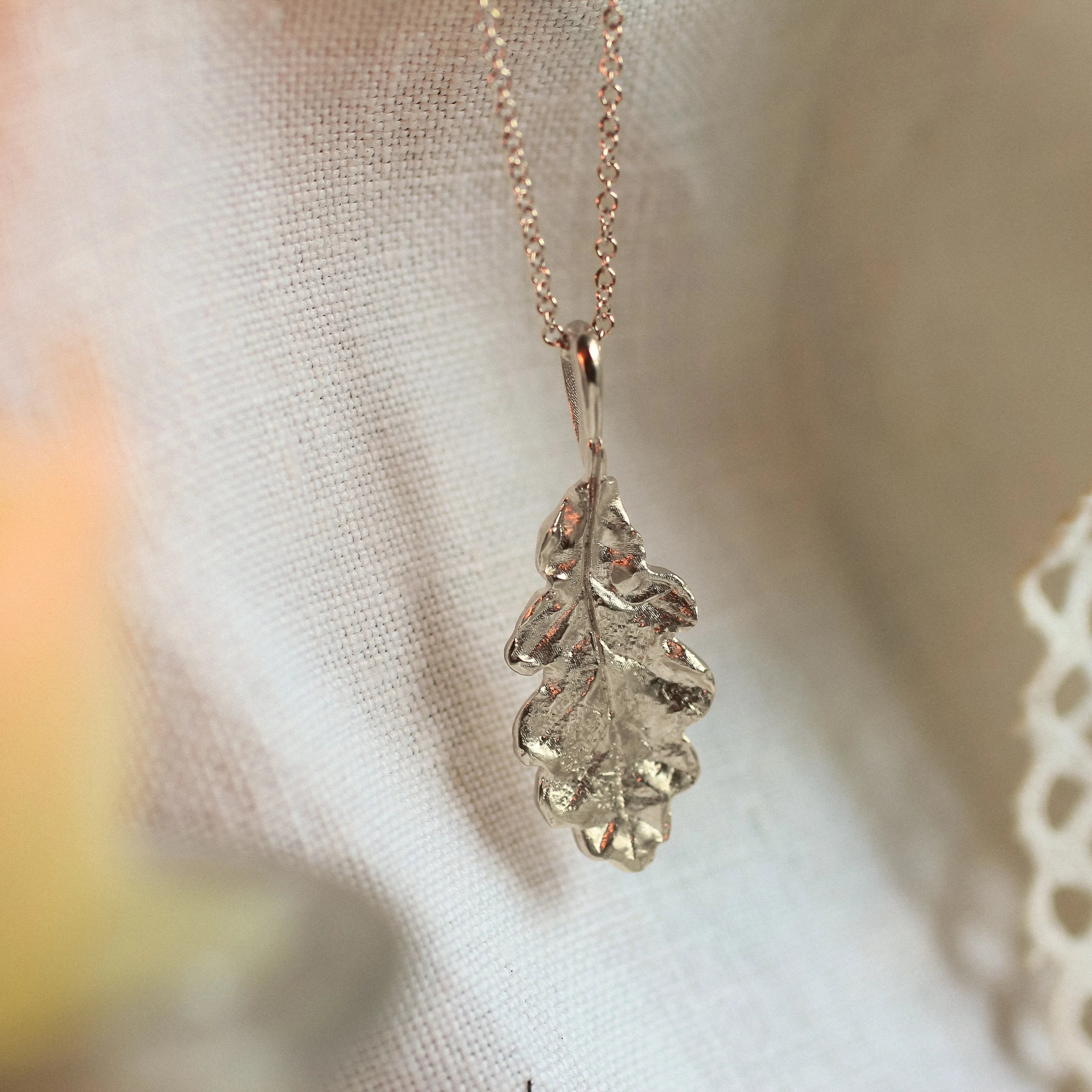 silver necklace with oak leaf pendant on neutral fabric
