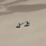 silver textured pebble stud earrings on beige surface with leaf shadows