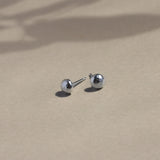 silver textured pebble stud earrings on beige surface with leaf shadows