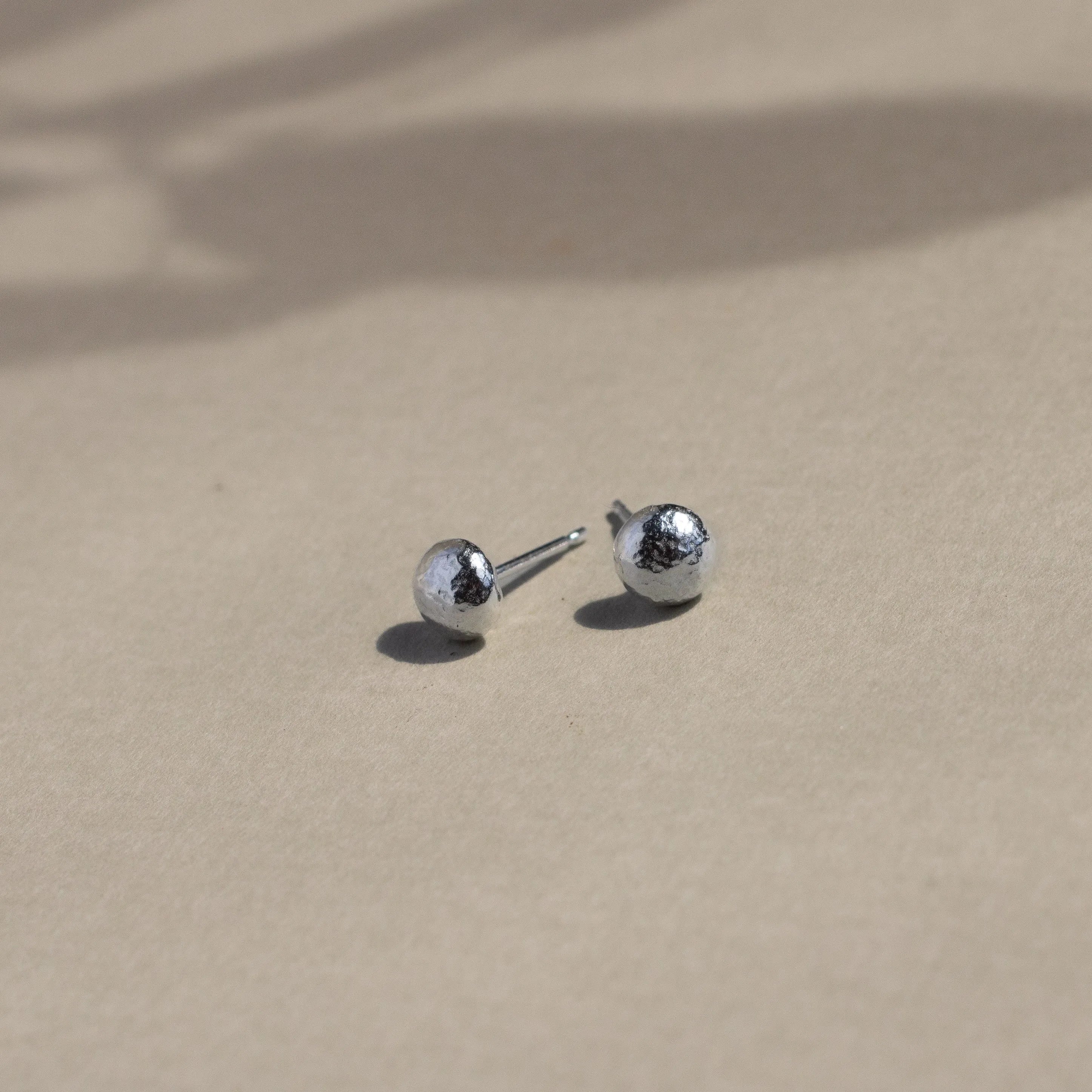 silver textured pebble stud earrings on beige surface with leaf shadows