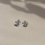 silver textured pebble-shaped earrings with butterfly backs on beige surface with leaf shadows