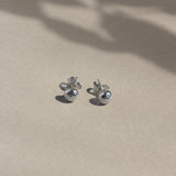 silver textured pebble-shaped earrings with butterfly backs on beige surface with leaf shadows