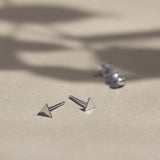 sterling silver triangle stud earrings with butterfly backs in background on beige surface with leaf shadows