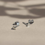 silver triangle stud earrings with butterfly backs on beige surface with leaf shadows