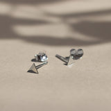 silver triangle stud earrings with butterfly backs on beige surface with leaf shadows