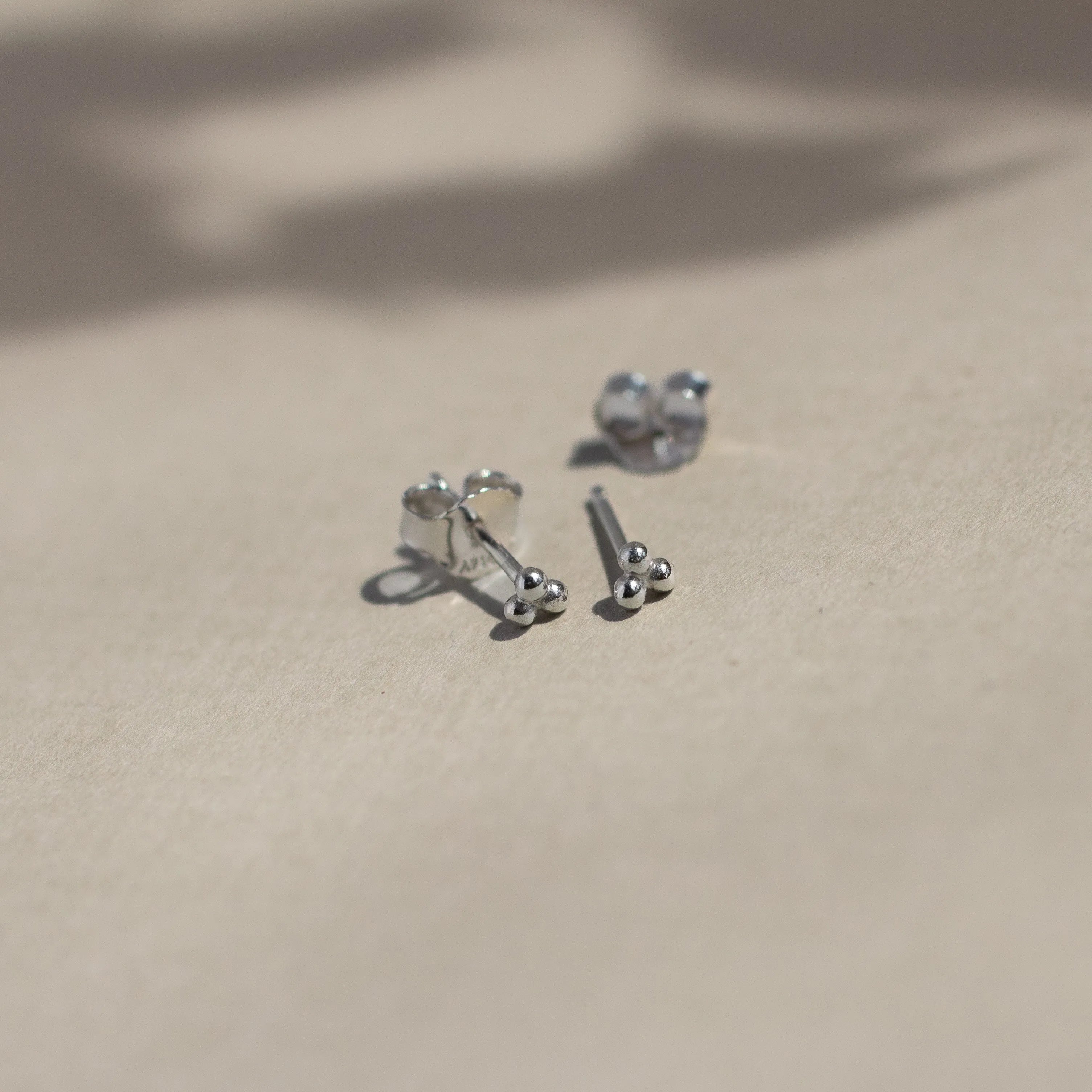 sterling silver triple dot stud earrings with butterfly backs on beige surface with leaf shadows
