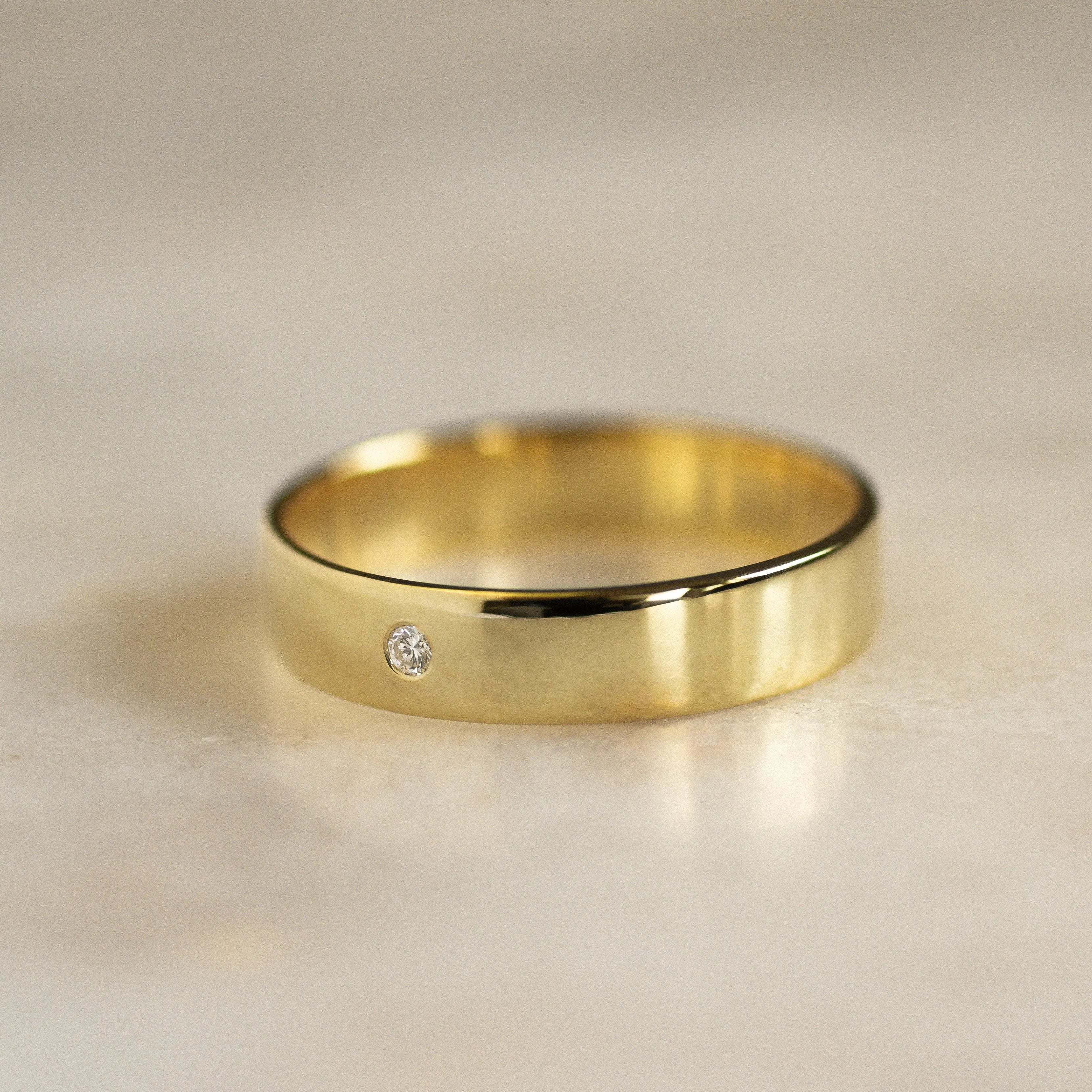 thick flat gold wedding band on marble surface with small round diamond