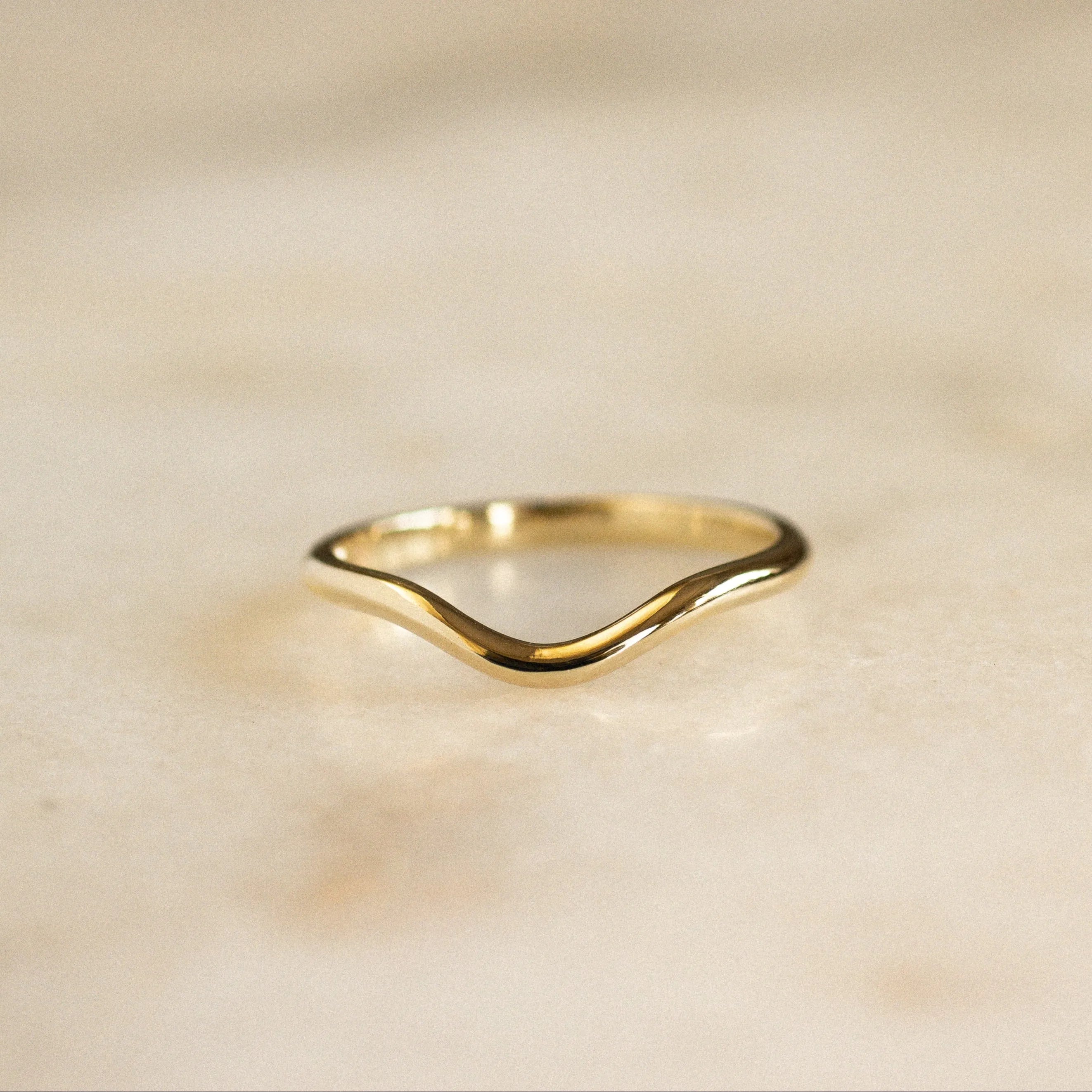 softly curved wedding ring in yellow gold on marble surface