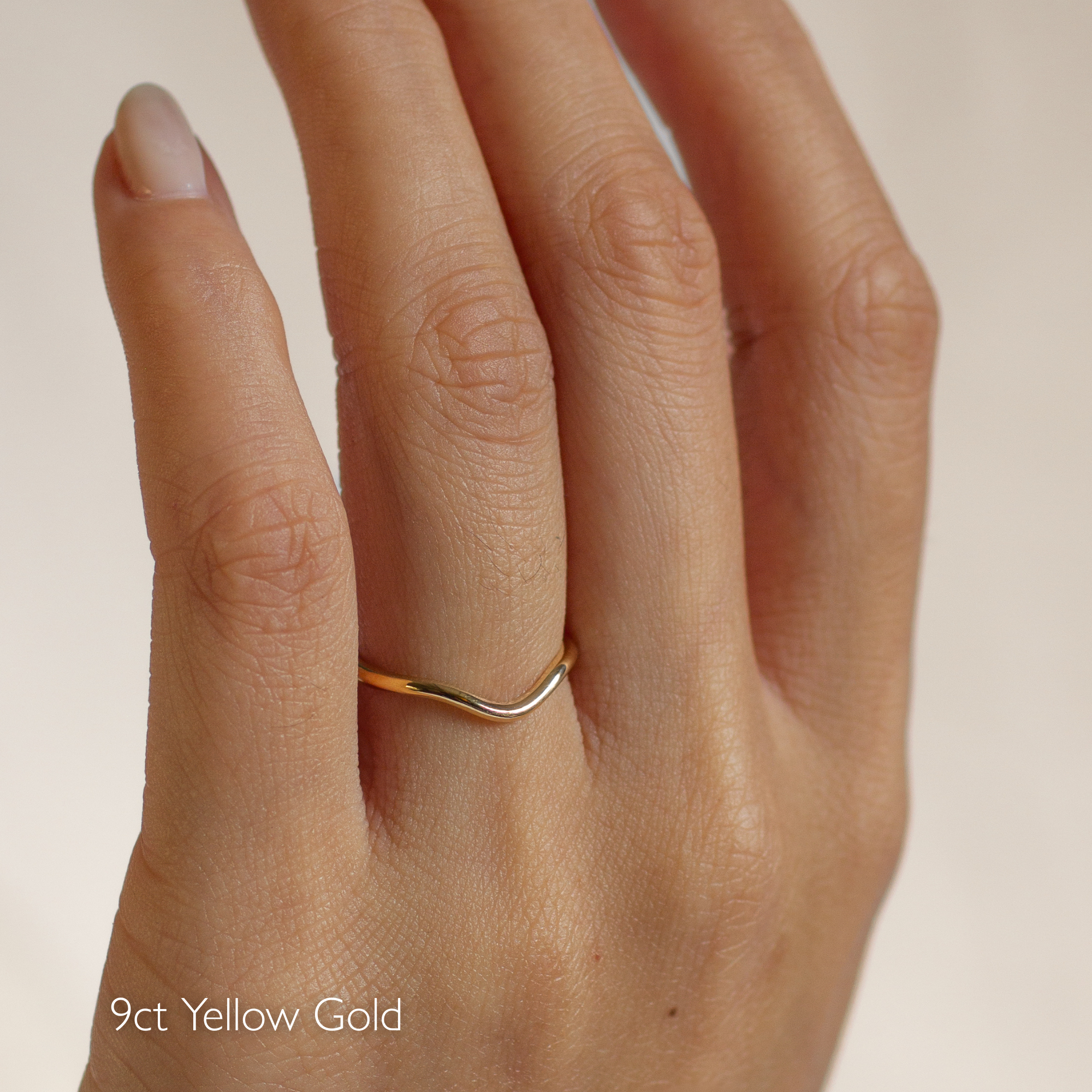 Slim curved curved wedding ring on a hand with '9ct Yellow Gold' text