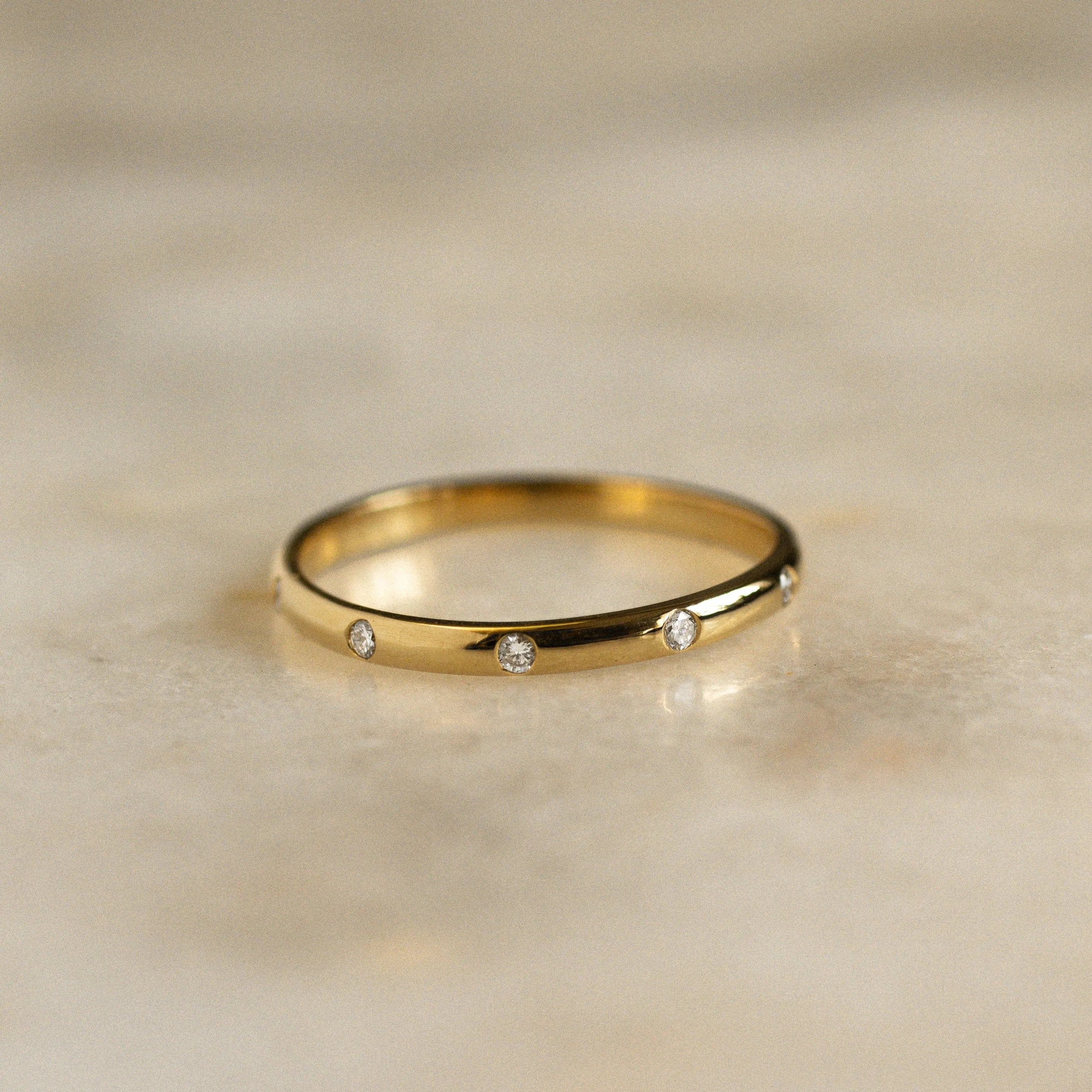 2mm gold wedding ring with small round diamonds spaced out around the band on marble surface
