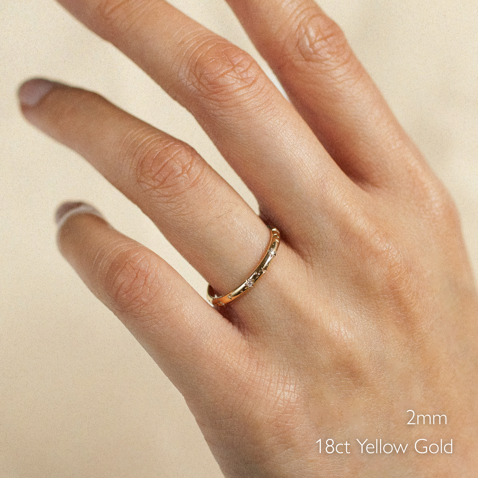 Hand wearing a 2mm wide 18ct yellow gold ring on a beige background