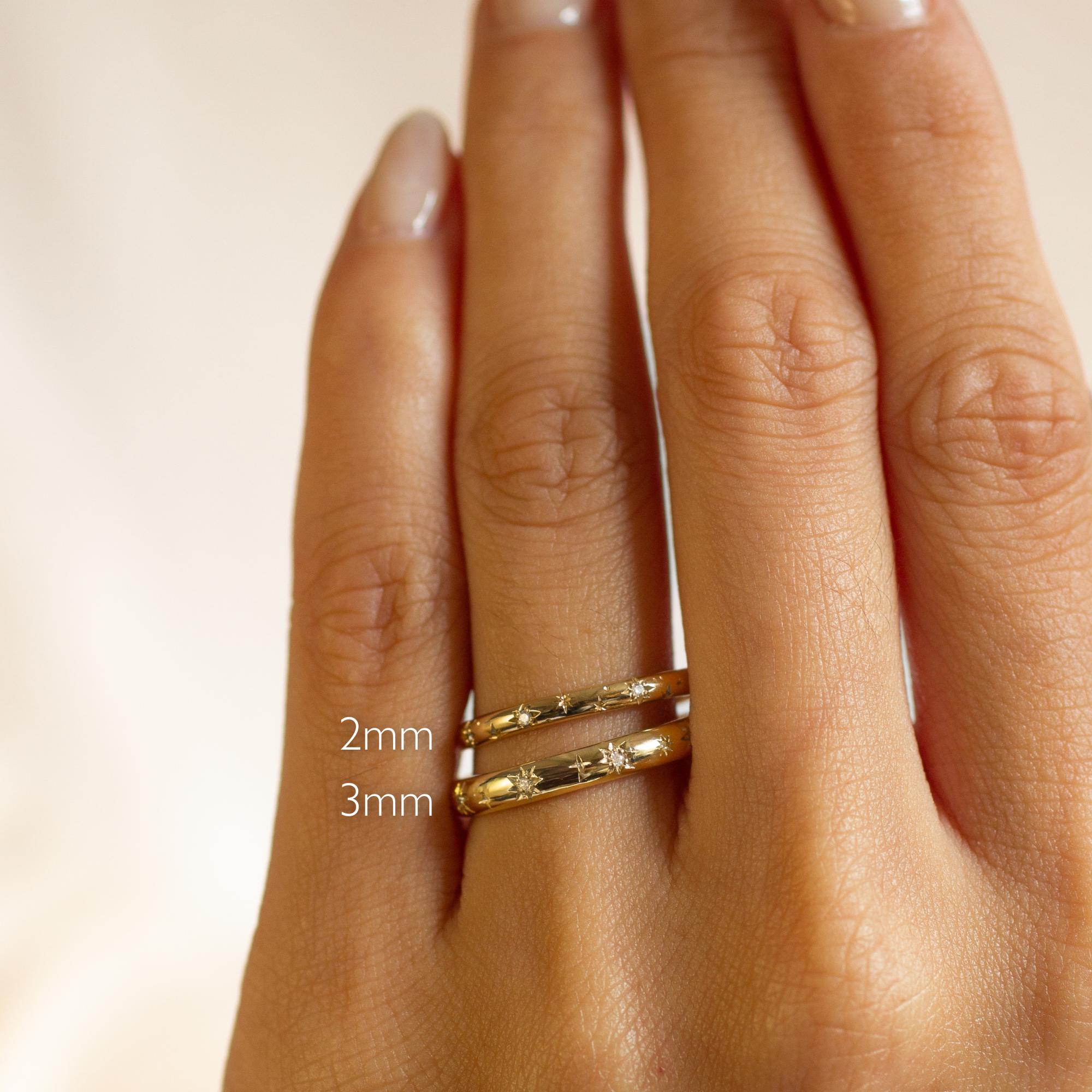 Gold star and diamond wedding rings on a hand with size labels '2mm' and '3mm' on a beige background