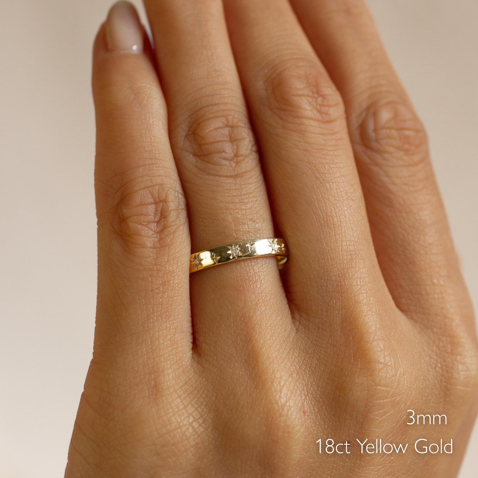 Gold flat wedding ring with star and diamond engraving on a hand with '18ct Yellow Gold' text