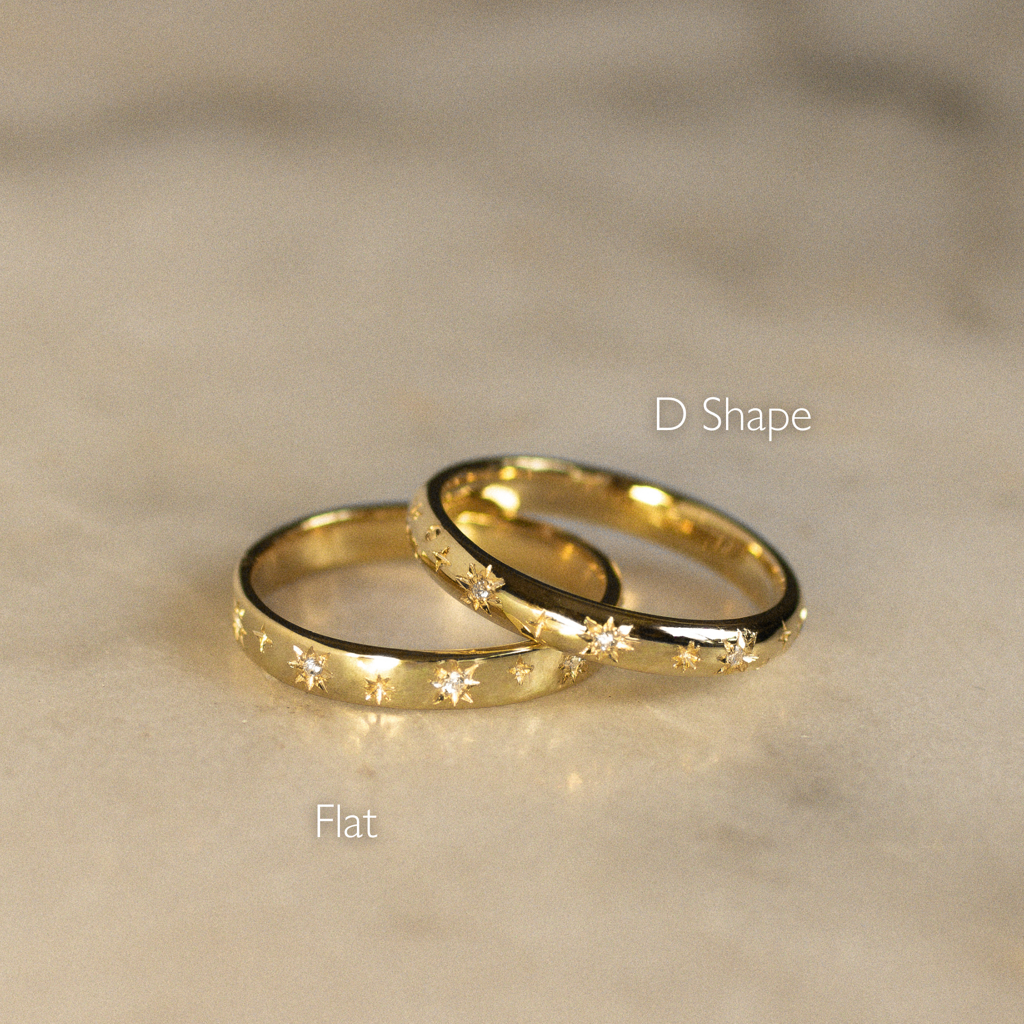 Two gold rings, one flat and one D-shaped, on a beige surface.