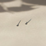 white gold tiny dot studs on beige surface with leaf shadows