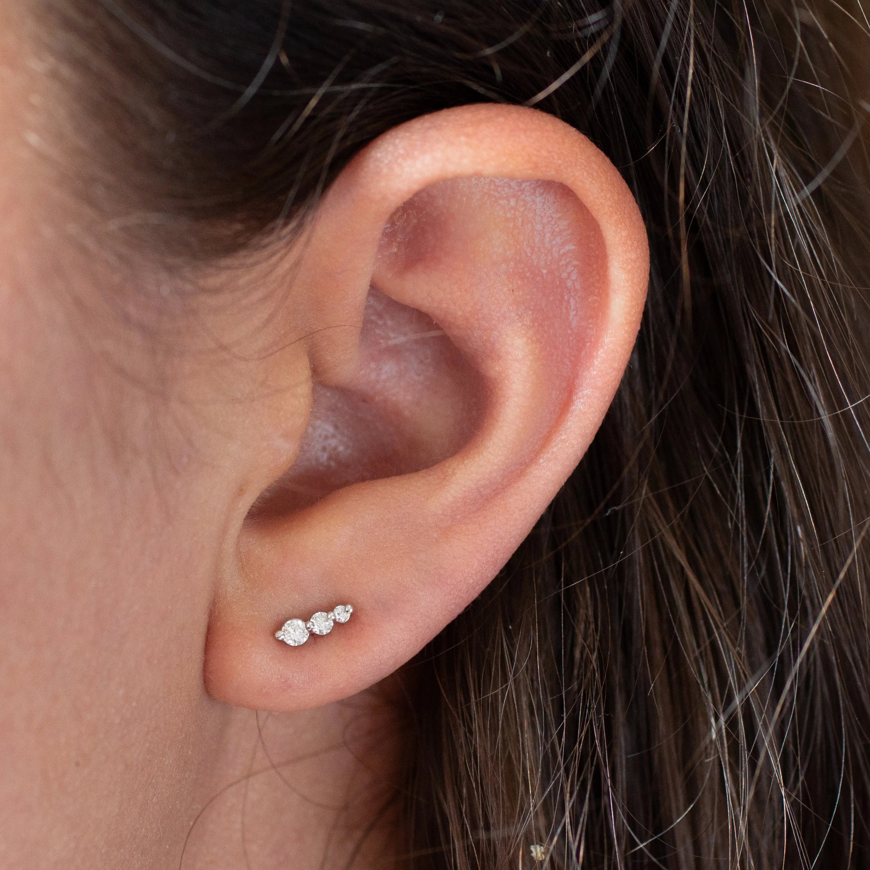 close up of ear wearing diamond climber stud earrings featuring three diamonds