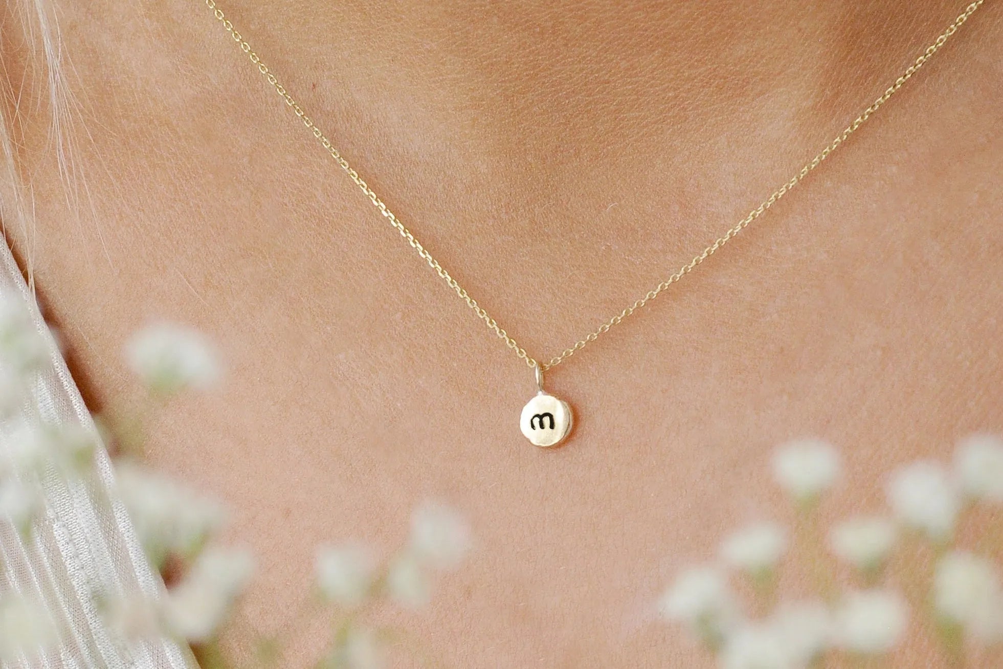 close up of inital necklace with 'm' being worn with flowers