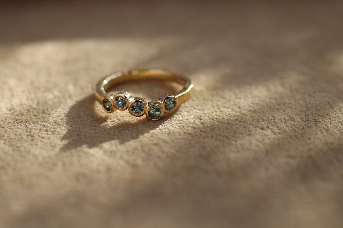 dainty engagement ring with five blue and green sapphires in a wave shape