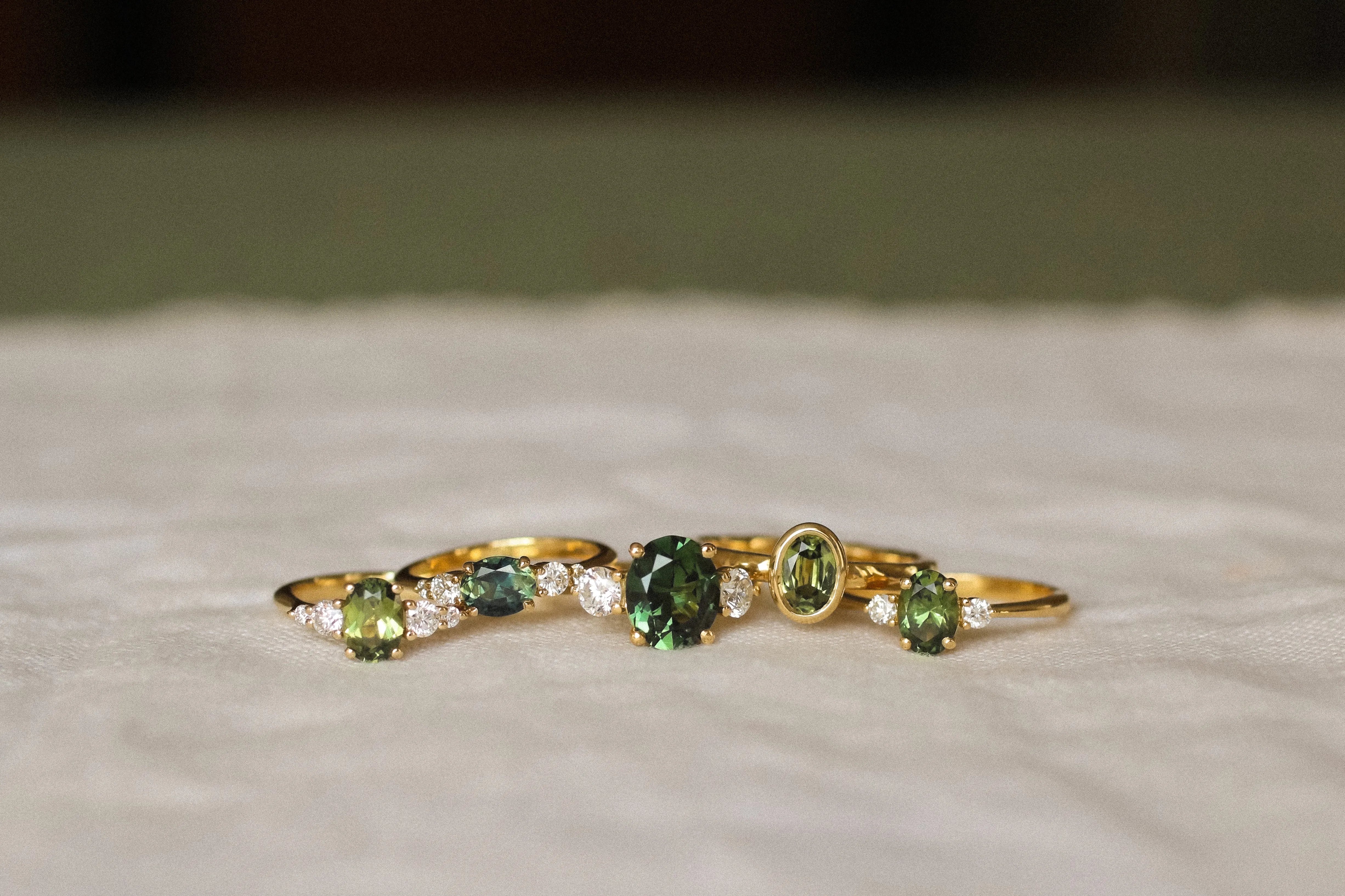 5 green sapphire engagement rings with diamonds on a beige surface and blurred background