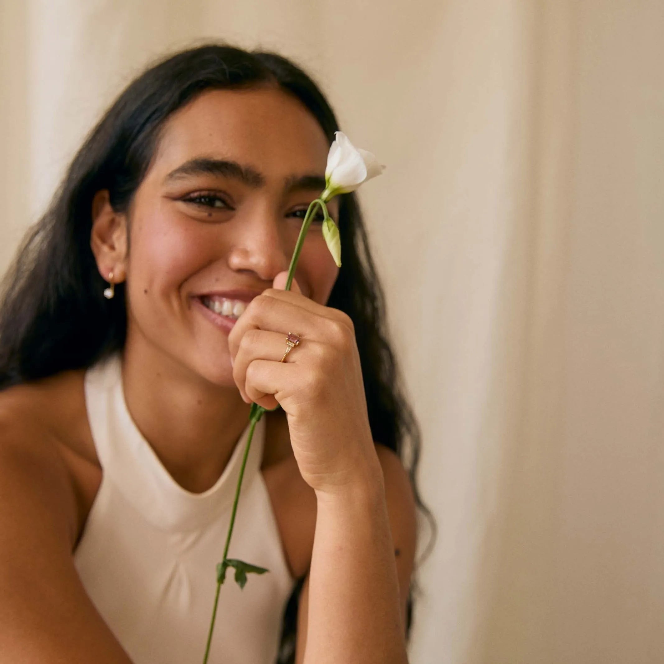 Woman holding a white flower against a beige curtain wearing a 5-stone pink sapphire engagement ring