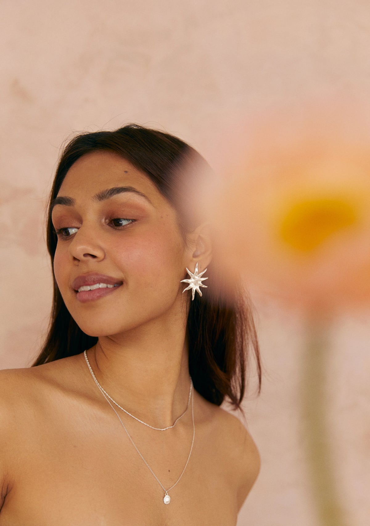 Brunette model wearing Silver Large Sun Earrings and silver necklaces, with blurred poppy flower in foreground