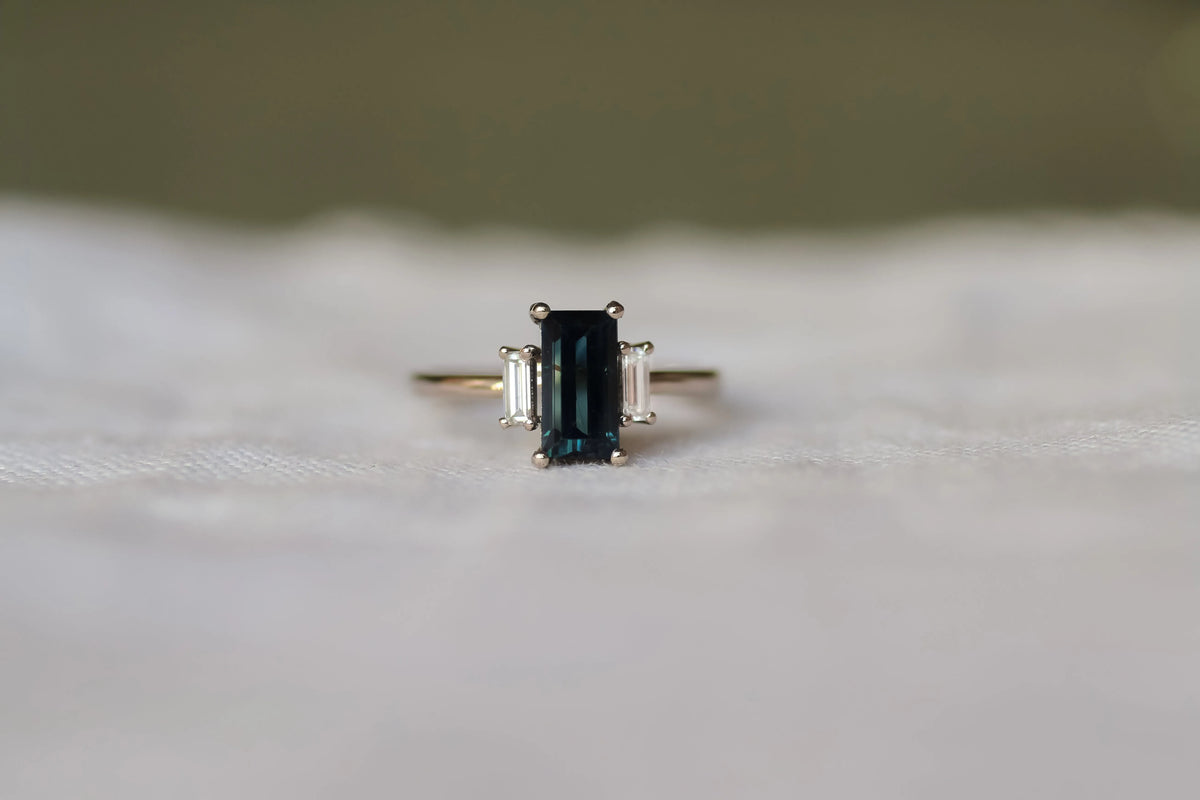 dark blue white gold bageuette cut engagement ring on a neutral surface